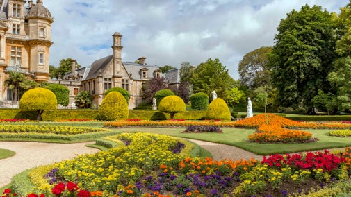 The parterre in summer at Waddesdon Manor, Buckinghamshire. Exterior view of the manor with decorative trees and flowerbeds filled with colourful flowers in the foreground.